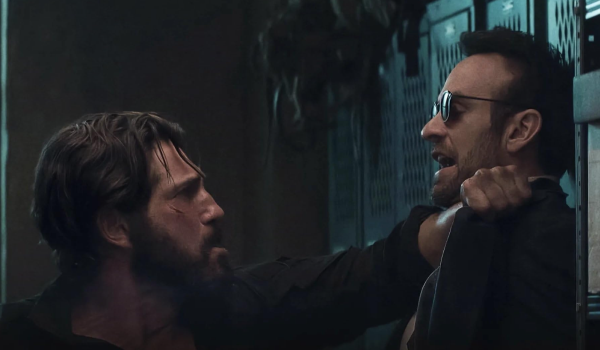 Jon Bernthal as Frank Castle aggressively pinning Charlie Cox as Matt Murdock against a row of metal lockers in a dimly lit basement