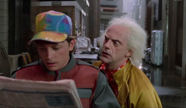 Movie still of Michael J. Fox as Marty McFly and Christopher Lloyd as Doctor Emmett Brown looking at a newspaper and talking about lawyers in the sci-fi movie Back to the Future Part II (1989)