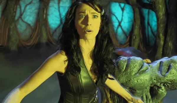 Still from Farscape featuring Claudia Black as Aeryn Sun with an expression of shock or surprise, set against the organic, glowing interior of the living ship Moya.