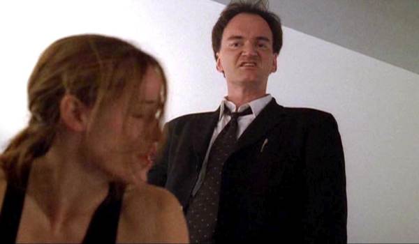 Quentin Tarantino as McKenas Cole and Jennifer Garner as Sydney Bristow in the TV series Alias, with Tarantino wearing a black suit and making a grimacing expression as he stands over a blurry Garner.