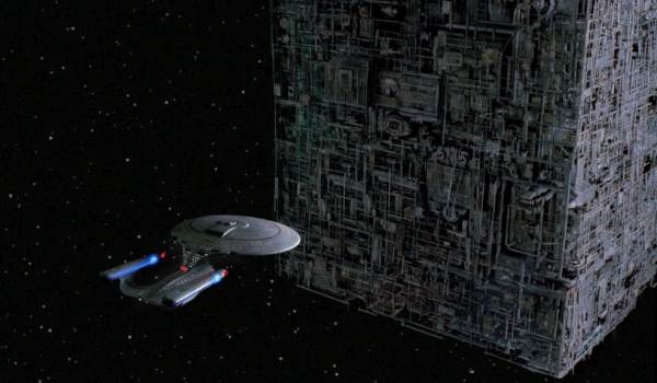 The Star Trek starship Enterprise-D dwarfed by a massive Borg Cube in deep space.