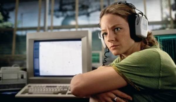 Jodie Foster as Dr. Ellie Arroway in the 1997 film Contact, wearing large headphones and looking intensely to the side while sitting in front of a vintage computer monitor.