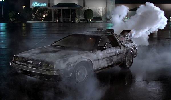 The DeLorean DMC-12 time machine parked on a street with its gull-wing doors open in a scene from the 1985 film Back to the Future.