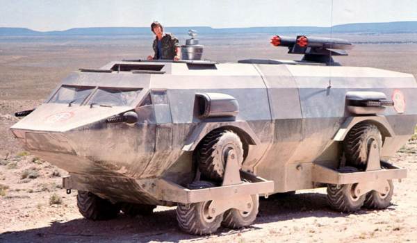  Side view of the Landmaster armored personnel carrier with a person standing in the top hatch, set against a desert landscape in Damnation Alley.
