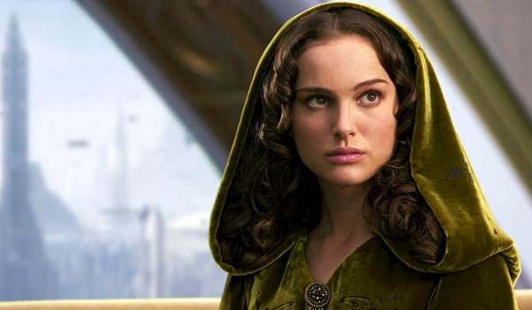 Natalie Portman as Padmé Amidala in Star Wars: Episode III – Revenge of the Sith, wearing a hooded green velvet cloak with a city skyline visible through a window in the background.
