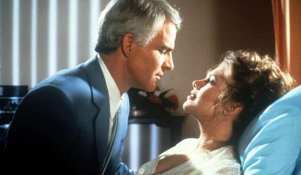 Steve Martin as Dr. Michael Hfuhruhurr and Kathleen Turner as Dolores Benedict in the 1983 film The Man with Two Brains, shown leaning in close to each other in a dimly lit room.