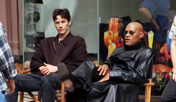 A behind-the-scenes photo from The Matrix (1999) featuring Keanu Reeves and Laurence Fishburne sitting in director's chairs between takes.