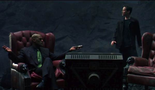 Morpheus (Laurence Fishburne) sitting in a red armchair gesturing towards Neo (Keanu Reeves) in a dark, surreal world of the Real from The Matrix (1999).