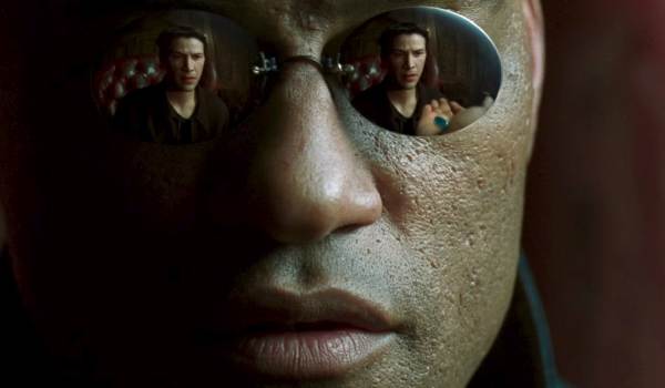 Extreme close-up of Morpheus (Laurence Fishburne) in The Matrix (1999), with the reflection of Neo (Keanu Reeves) reaching for the red pill visible in his sunglasses.