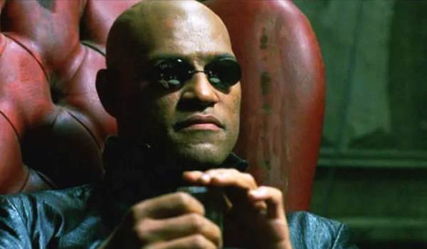 Laurence Fishburne as Morpheus in The Matrix (1999), wearing his iconic pince-nez sunglasses and a black leather coat while sitting in a red leather chair.
