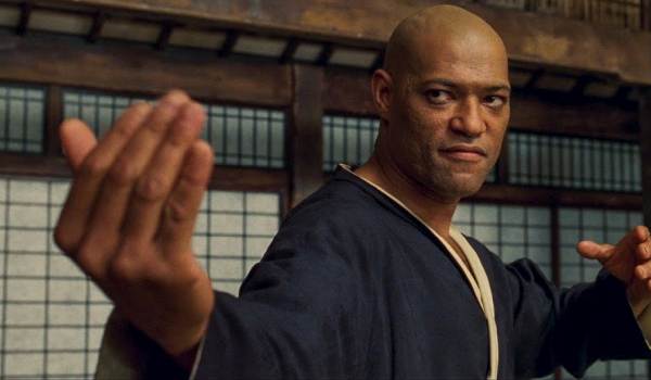 Laurence Fishburne as Morpheus in The Matrix (1999), wearing a black gi and holding a martial arts stance during the dojo sparring scene with Neo.
