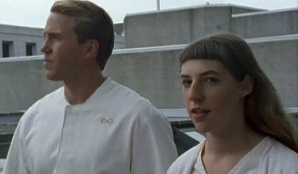 Mayim Bialik and Brian Krause wearing white, minimalist futuristic tunics in an outdoor setting from the science fiction anthology series Welcome to Paradox.