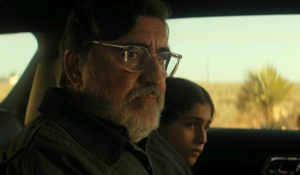 Alfred Molina as Sam Cooper in clear glasses looks out a car window in a desert landscape in Netflix's sci-fi show The Boroughs.