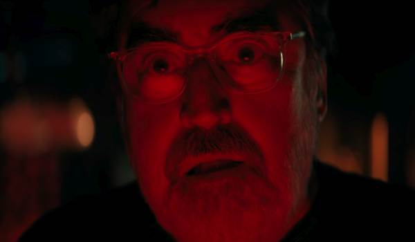 A close-up shot of Alfred Molina looking wide-eyed and shocked under intense red lighting in Netflix's The Boroughs.