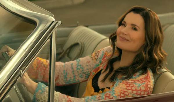 Geena Davis as Renee is smiling while driving a convertible car in a scene from Netflix's The Boroughs.