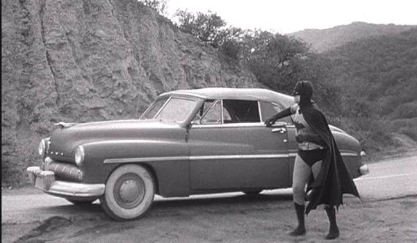 Lewis Wilson as Batman in the 1949 Batman serials standing next to the 1939 Cadillac Series 75 convertible Batmobile on a dirt road. 