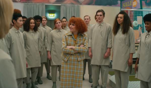 Natasha Lyonne as the Store Manager standing with crossed arms among a large group of people wearing matching light grey uniforms in the movie Klara and the Sun.