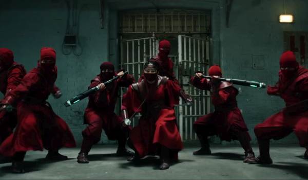 A group of Hand ninjas dressed in red uniforms and masks striking battle poses in front of a metal cell door in a scene from Spider-Man: Brand New Day.