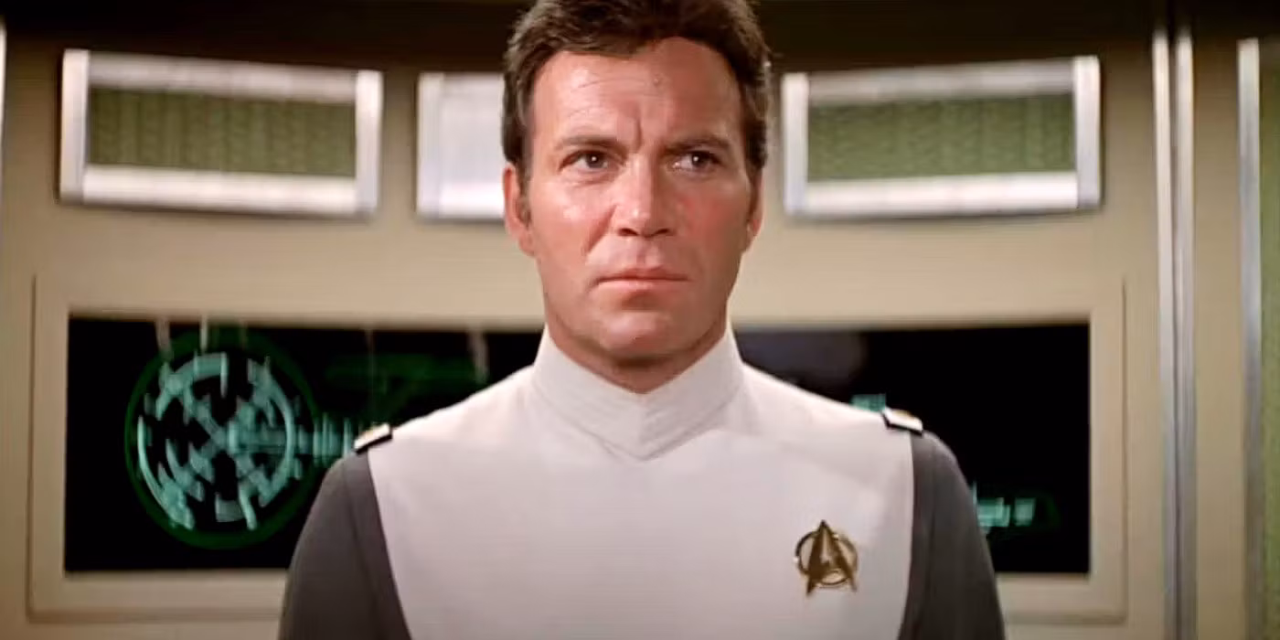A medium close-up of William Shatner as Admiral James T. Kirk wearing a white and gray Starfleet uniform on the bridge of the starship Enterprise.