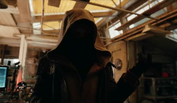 A mysterious figure stands with his face completely obscured in shadow beneath a large hood inside a cluttered workshop scene from Spider-Man: Brand New Day.