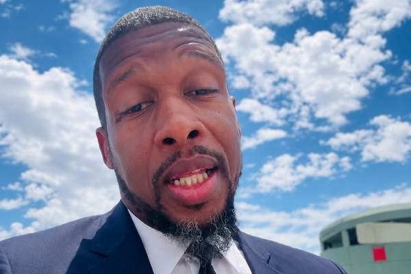 Comic book creator Lonnie “Lō” Plater in an outdoor interview headshot wearing a suit against a cloudy blue sky.