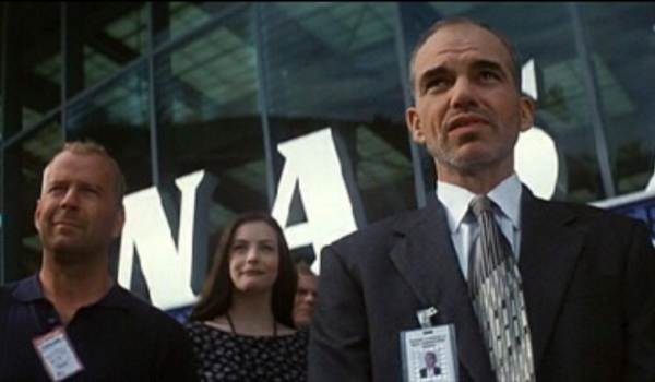 Bruce Willis as Harry Stamper, Liv Tyler as Grace Stamper, and Billy Bob Thornton as Dan Truman standing in front of the NASA logo in the sci-fi disaster film Armageddon.