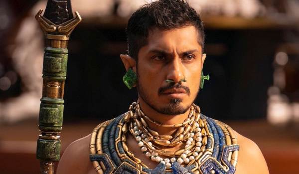 Tenoch Huerta Mejía as Namor wearing ornate jewelry and holding a spear in the Marvel movie Black Panther: Wakanda Forever.