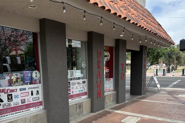 Exterior storefront of Drawn to Comics in Glendale featuring window displays of comic books, publisher logos, and red vertical lettering on the pillars.