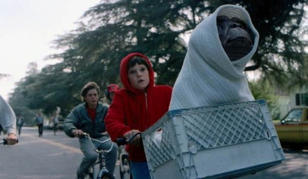 Henry Thomas as Elliott rides a bicycle with E.T. wrapped in a white blanket in the classic American sci-fi movie E.T. the Extra-Terrestrial.