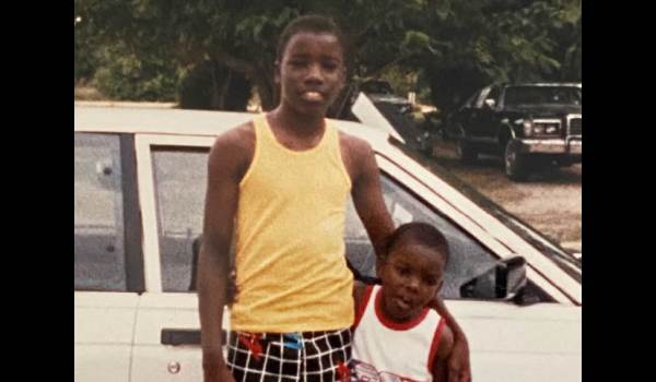 A vintage photograph of actor Mike Colter as a child standing next to a younger child in front of a white car.